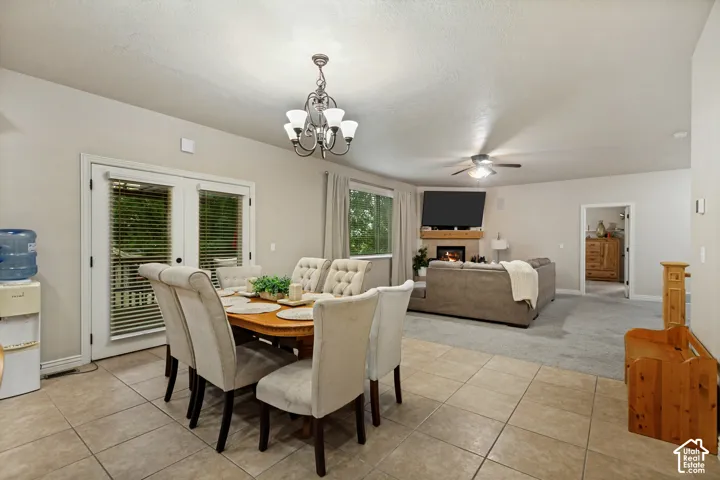 Open-concept living space featuring ceramic tile flooring, a fireplace with a wood mantel, a multi-light chandelier, and glass-paned doors