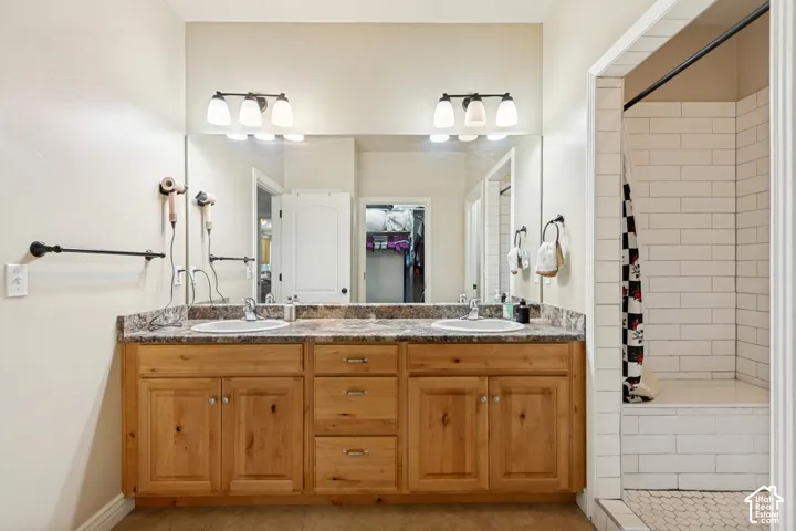 Double vanity with stone-finish countertop, dual drop-in sinks, natural-finish wood cabinetry, full-width vanity mirror, and subway-tile shower surround