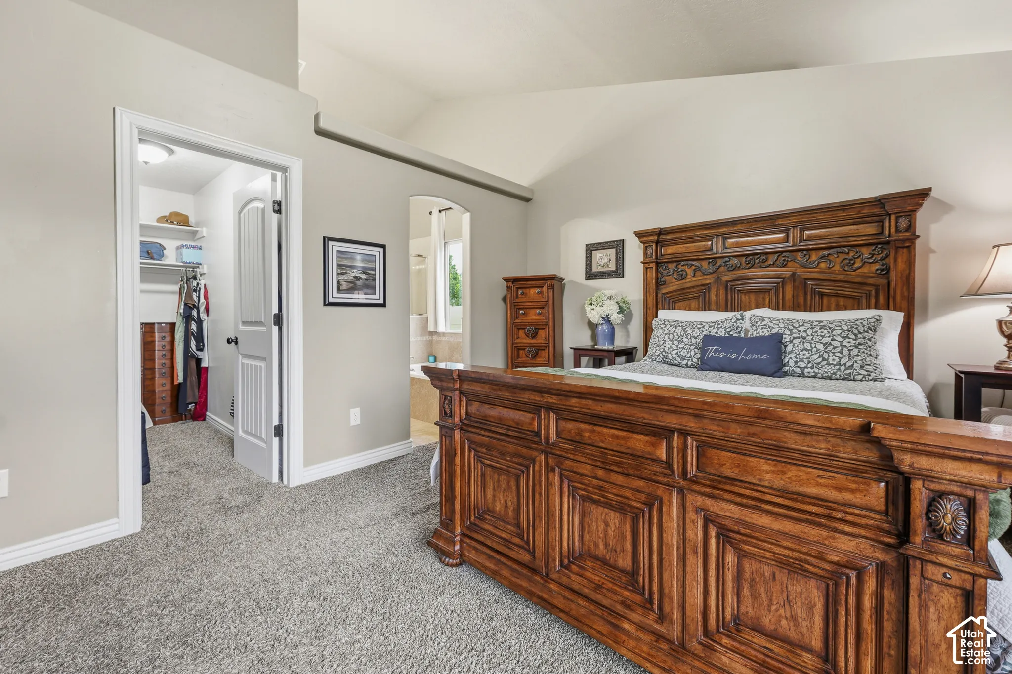 Vaulted ceilings, neutral wall paint, carpeting, and an arched doorway leading to a secondary room