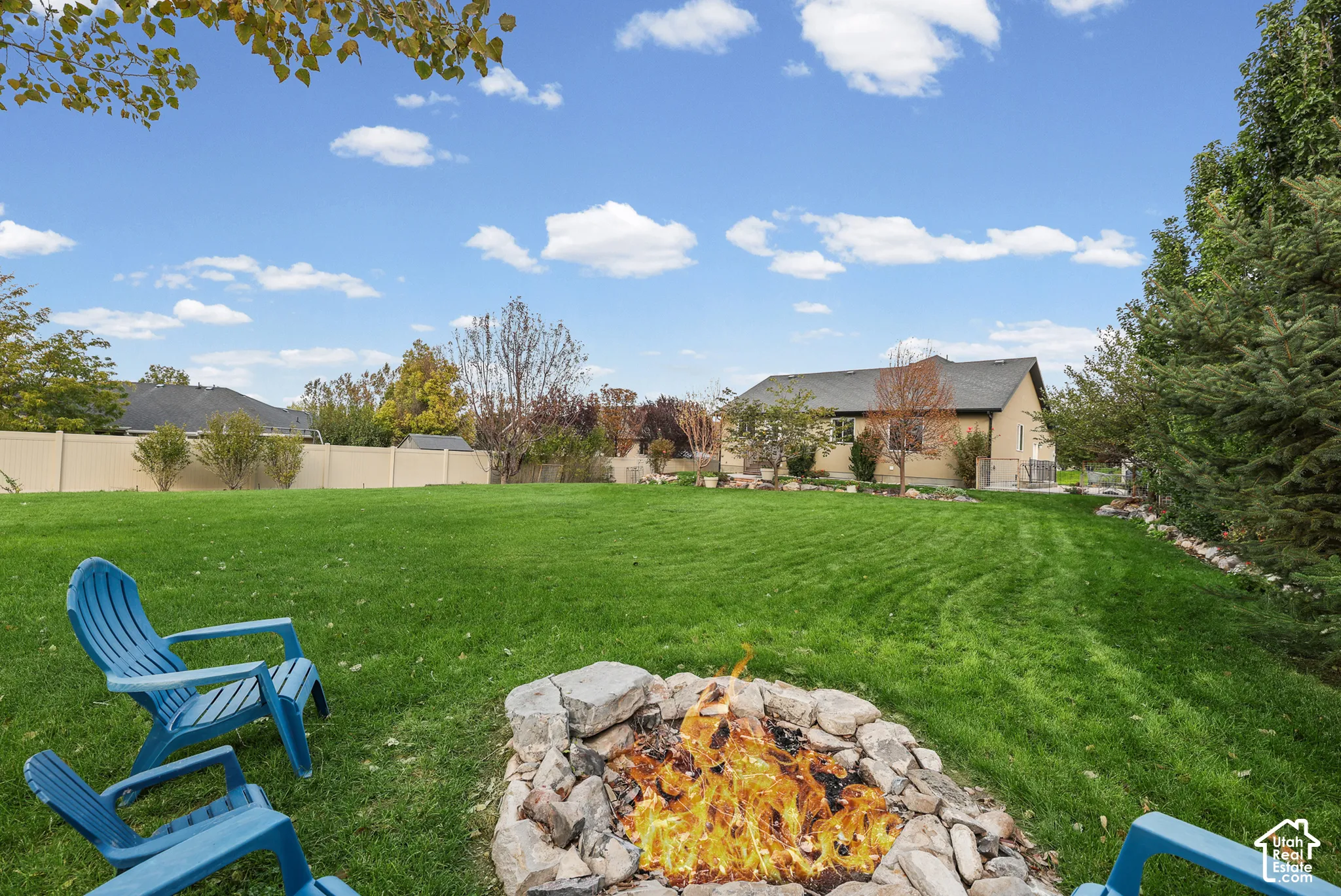 Expansive backyard featuring a stone-lined fire pit, manicured lawn, and privacy fencing