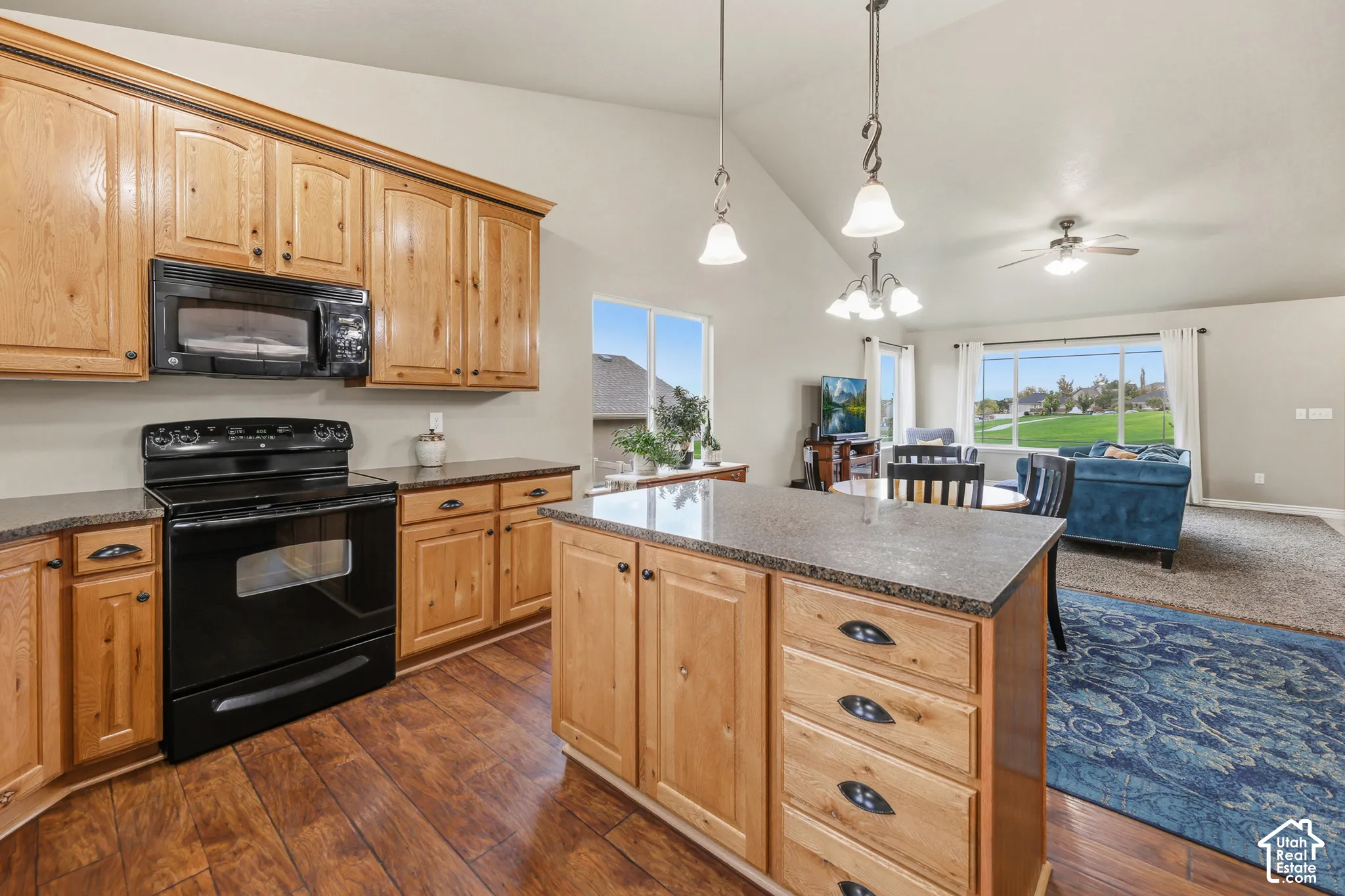 Kitchen featuring wood cabinetry, a center island with countertop seating, black appliances, wood-finish flooring, and vaulted ceilings