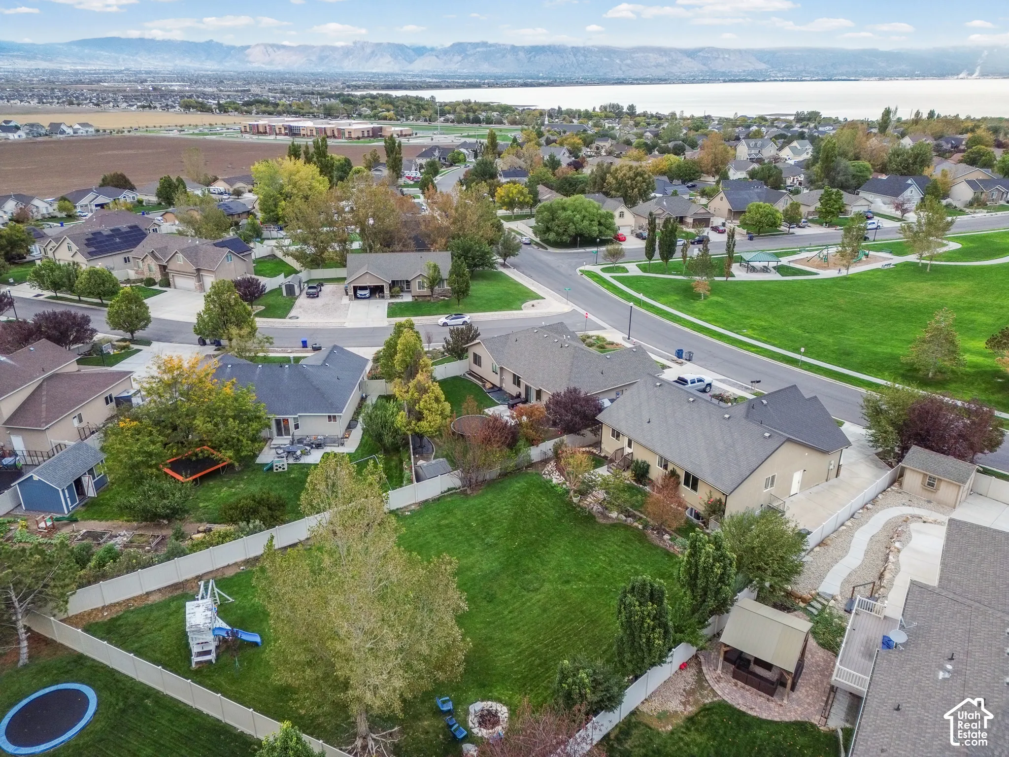 Aerial perspective of a fenced backyard featuring a manicured lawn, mature trees, a paver patio with a built-in pavilion, and a mountain range backdrop