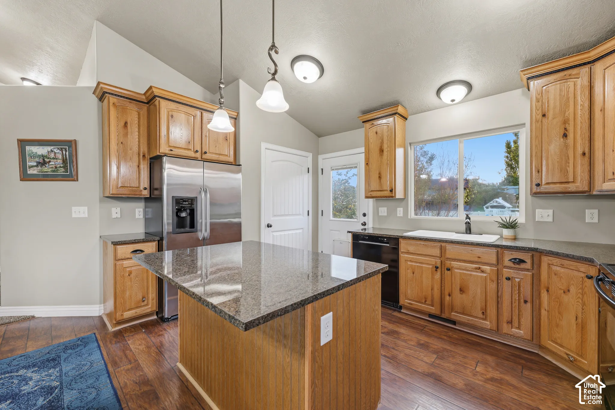 Kitchen featuring wooden cabinetry, stone-surface countertops, central island, dual-basin sink, and overhead pendant lighting
