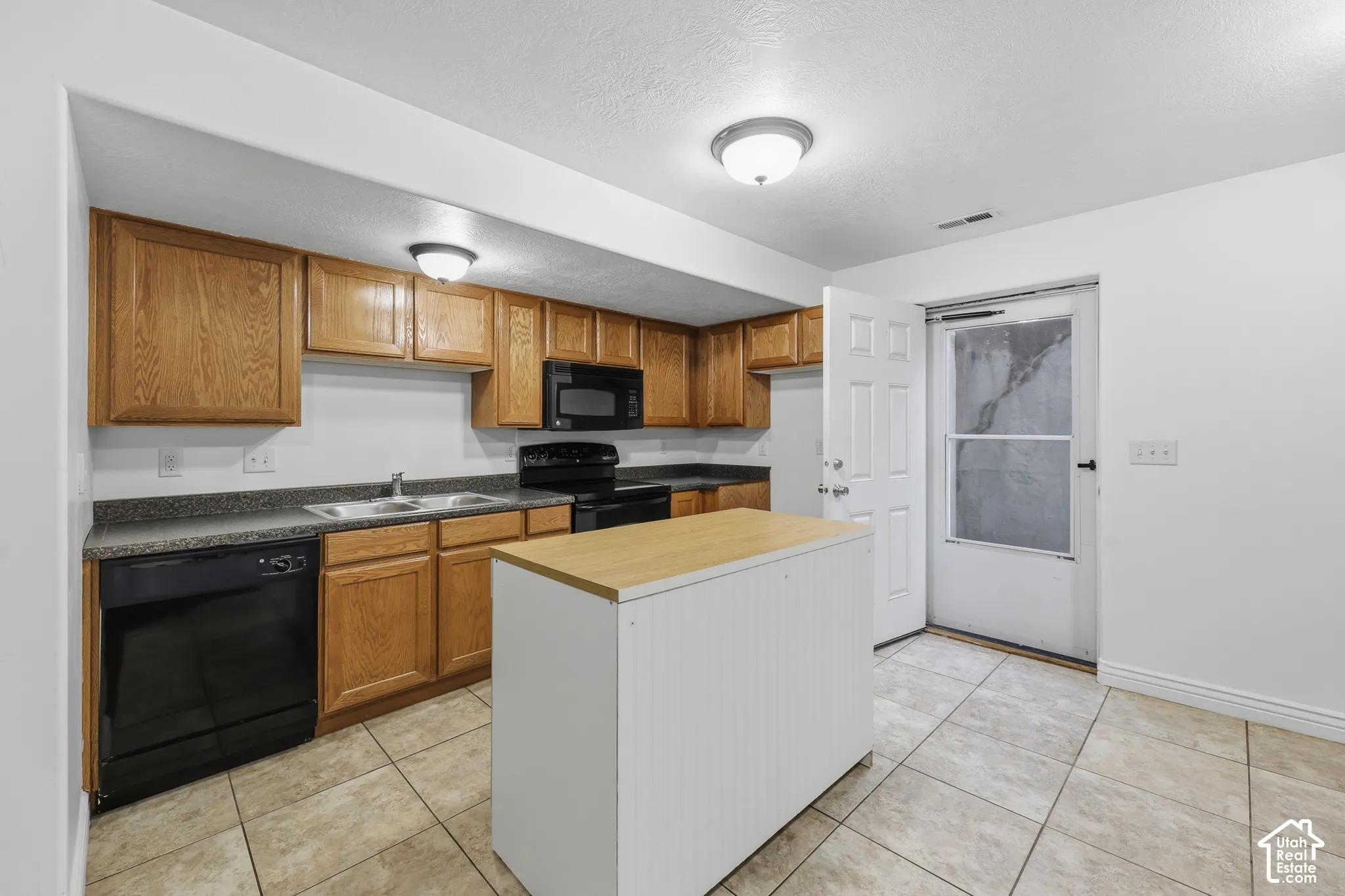 Kitchen featuring wood cabinetry, a center island with a wood-finish countertop, dark-toned appliances, solid-surface countertops, and tile flooring