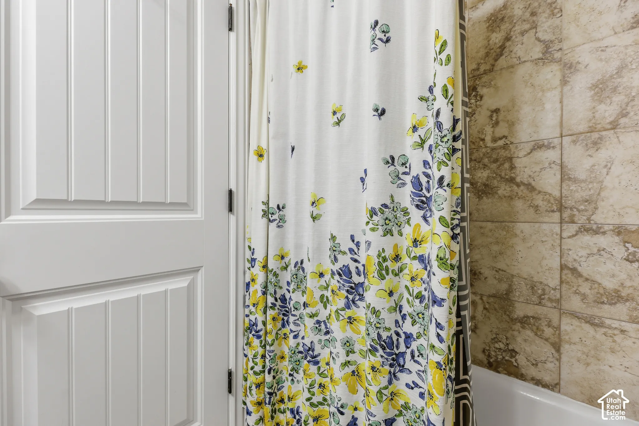 Elegant bathroom featuring a decorative shower curtain with blue and yellow floral patterning, polished chrome shower fixtures, and neutral tile flooring and surround walls in warm earth tones
