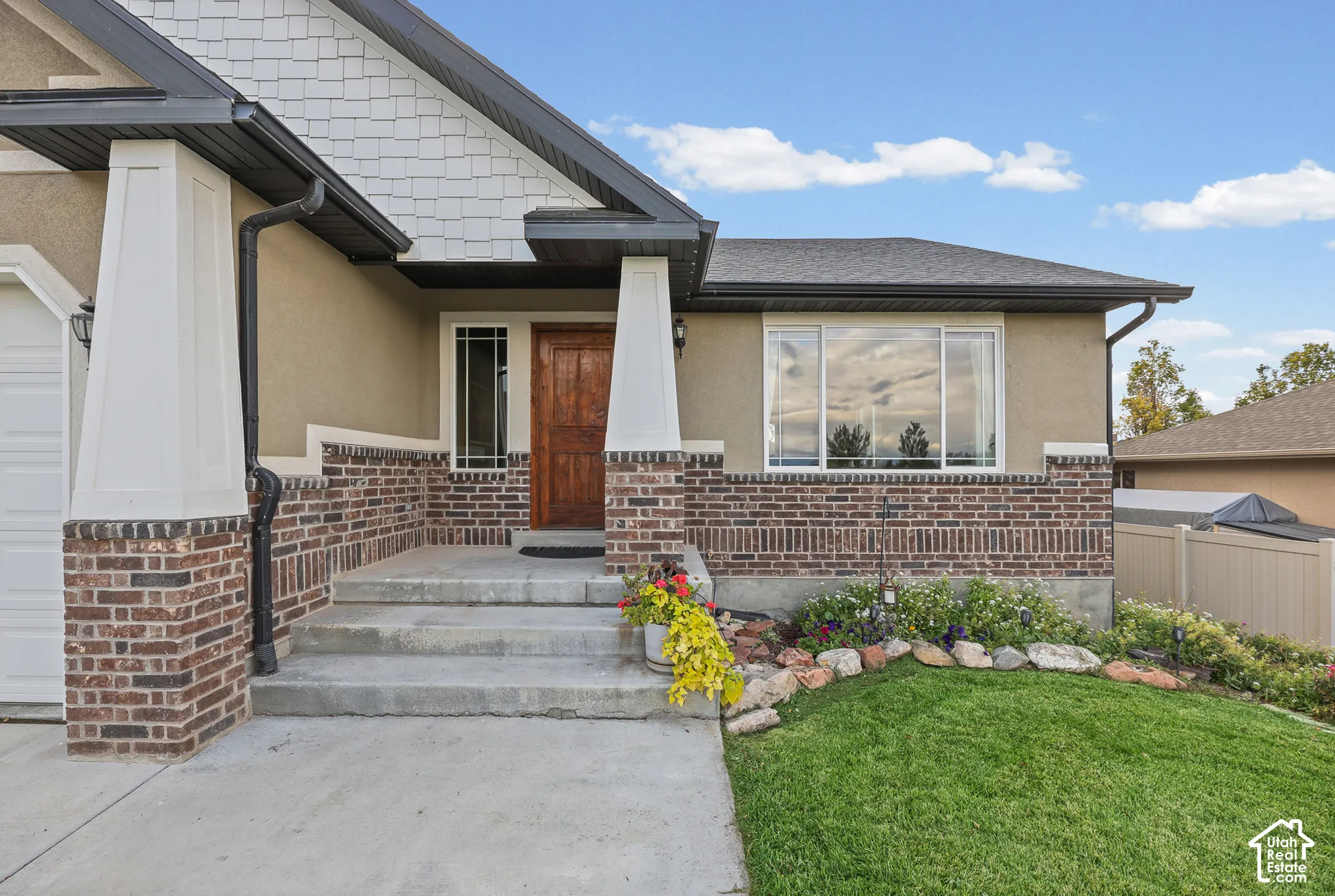 Exterior facade featuring a combination of stucco and masonry brick siding, shake-style gable detailing, a prominent covered entryway with tapered columns, and a wood-finish front door