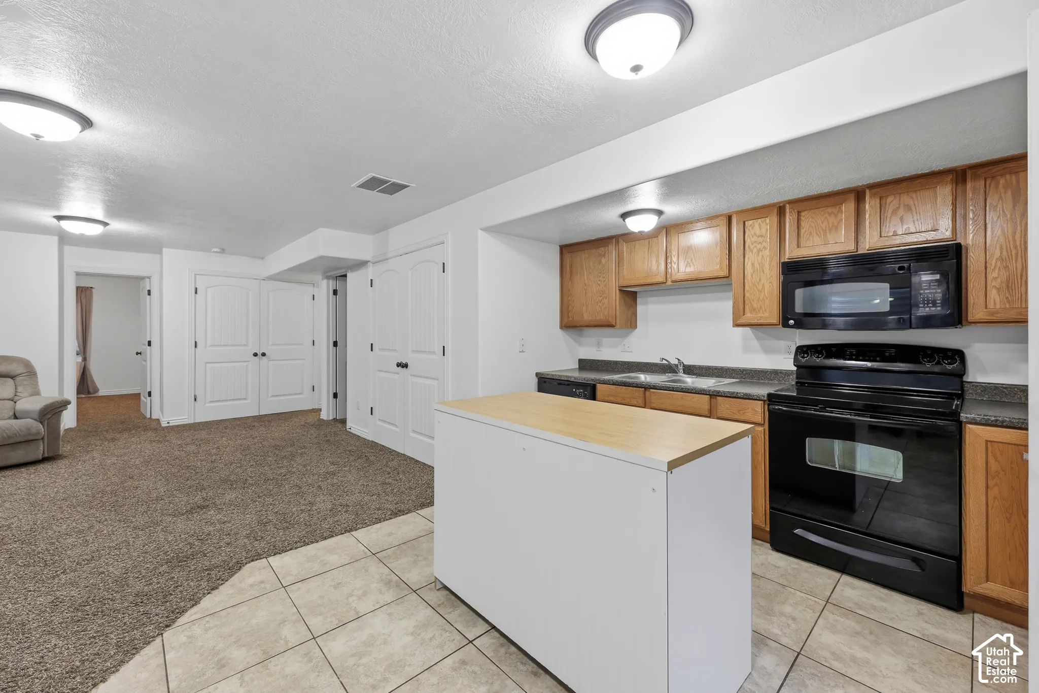 Kitchen featuring wood cabinetry, a standalone island with a wood-finish countertop, black appliances, tile flooring, and flush-mount ceiling lighting