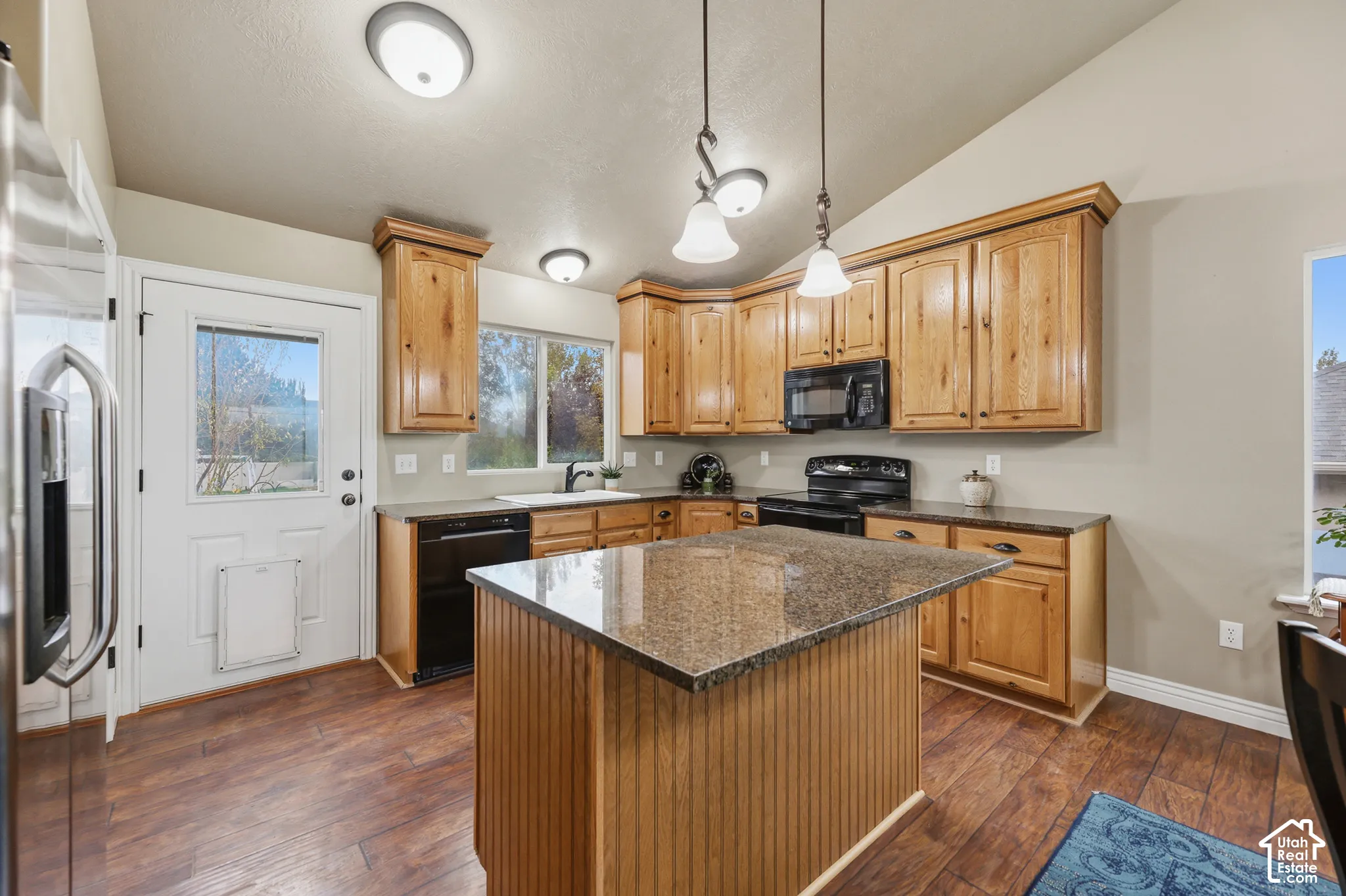 Kitchen featuring wood cabinetry, stone countertops, central island, wood-finish flooring, and pendant lighting