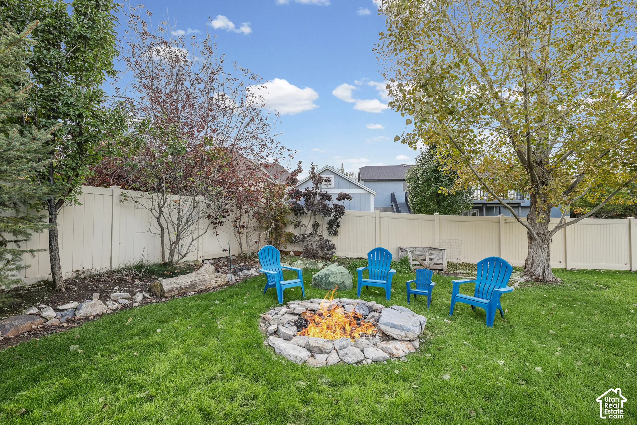 Backyard featuring a stone fire pit, vinyl privacy fencing, manicured lawn, and mature trees