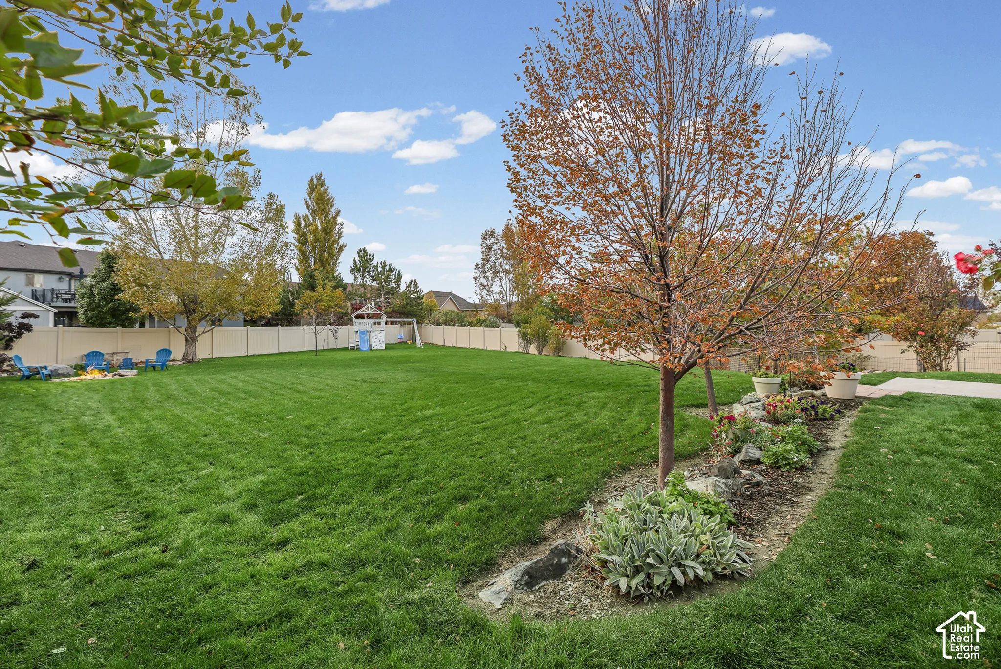 Spacious backyard featuring a manicured lawn, established landscaping, decorative rock edging, and a vinyl privacy fence