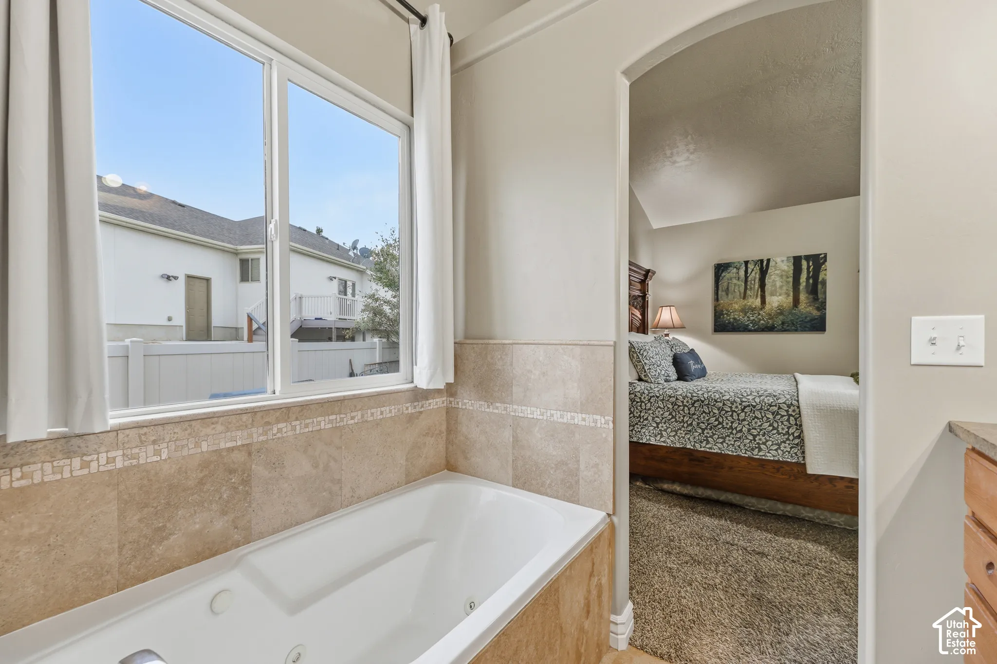 Jetted soaking tub with tile surround, decorative tile accent border, and large window