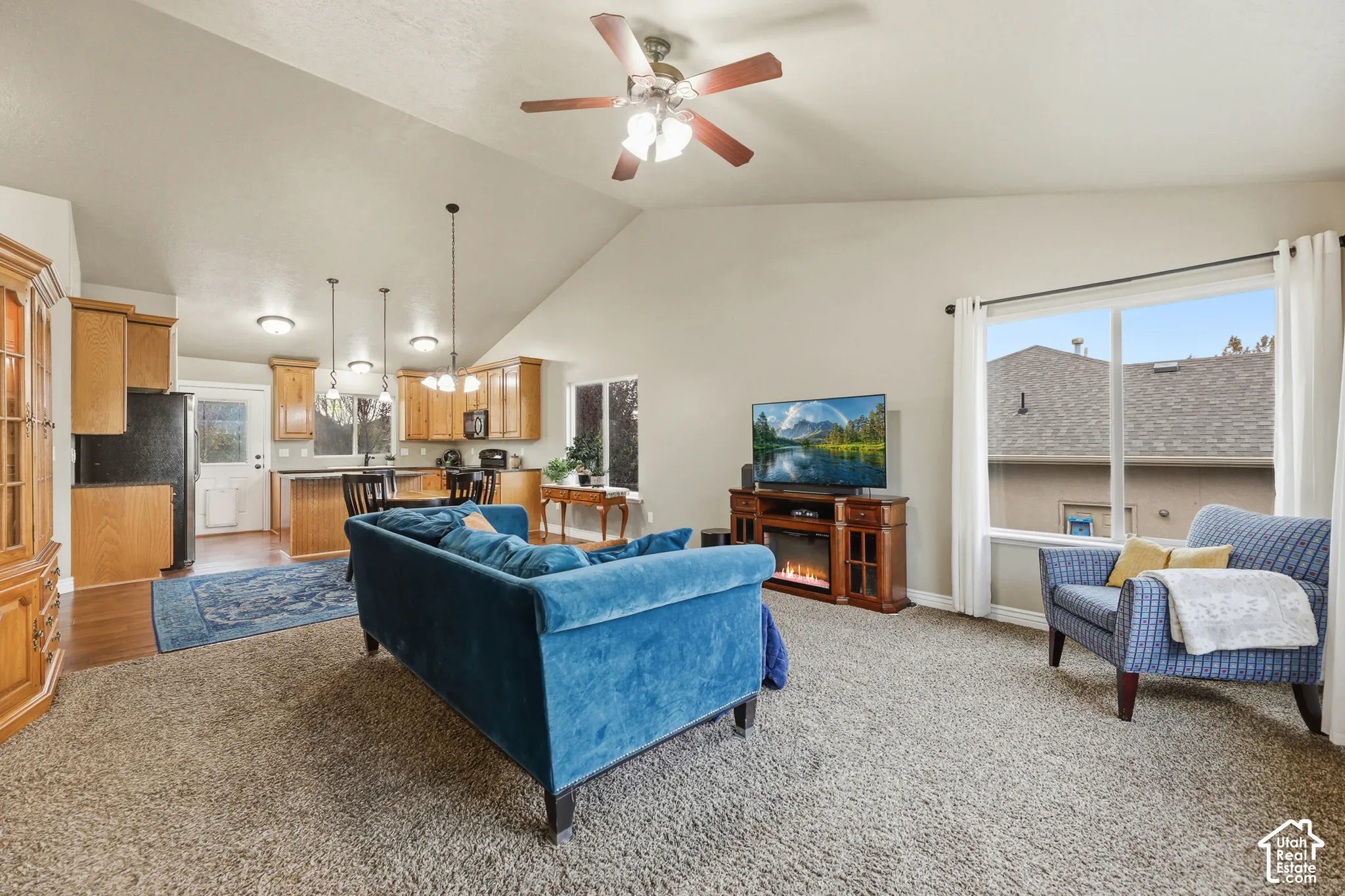Vaulted ceilings featuring a central ceiling fan, kitchen cabinetry with wood finishes, and large windows providing natural light