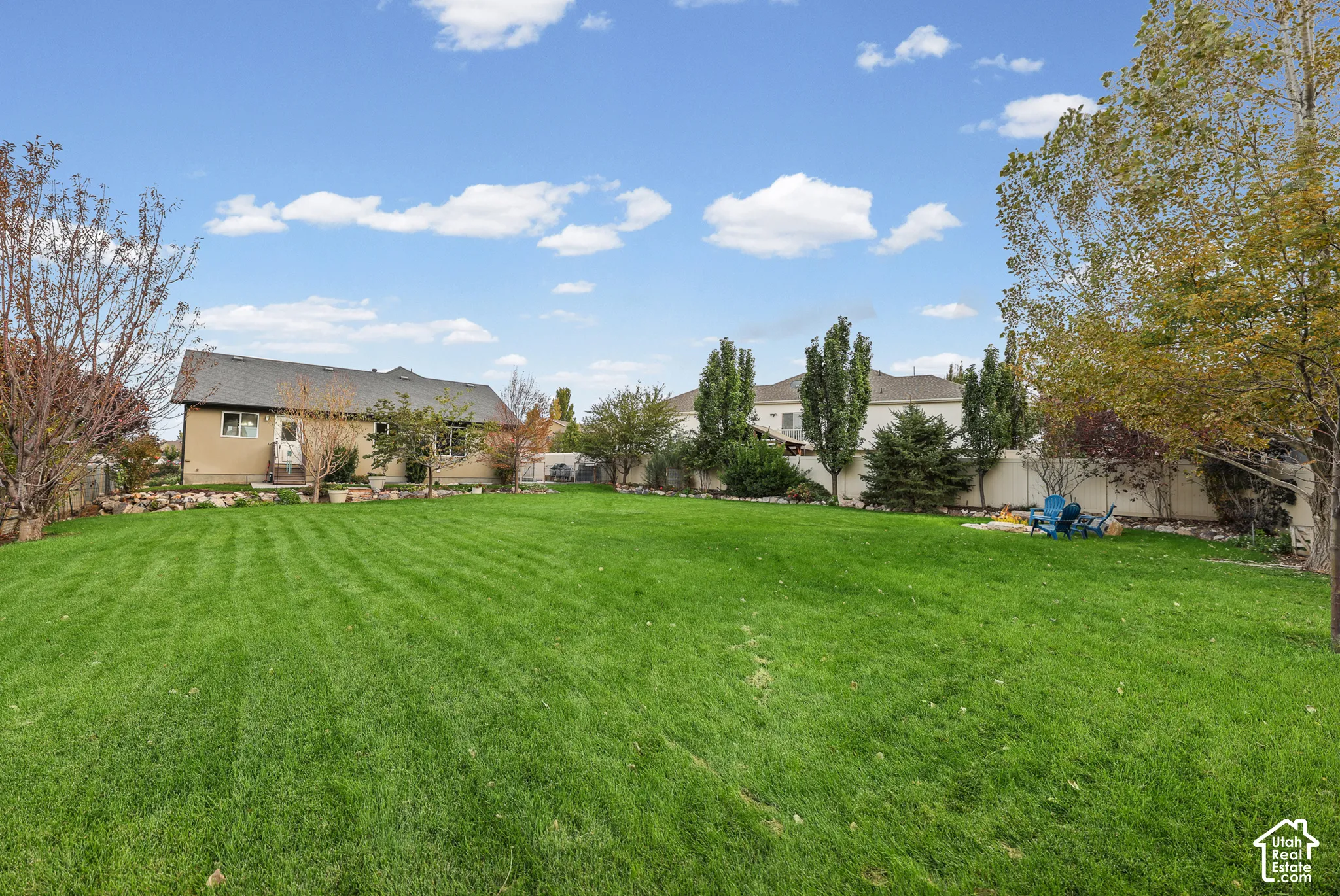 Expansive backyard featuring a large grass lawn, mature trees, stone landscaping borders, and perimeter fencing