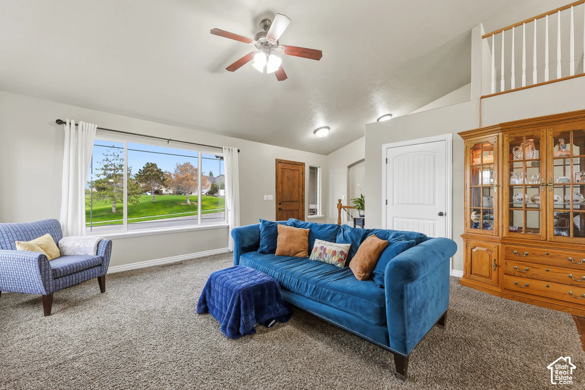 Vaulted ceilings, large picture window, ceiling fan with integrated lighting, built-in cabinetry, and interior balcony railing