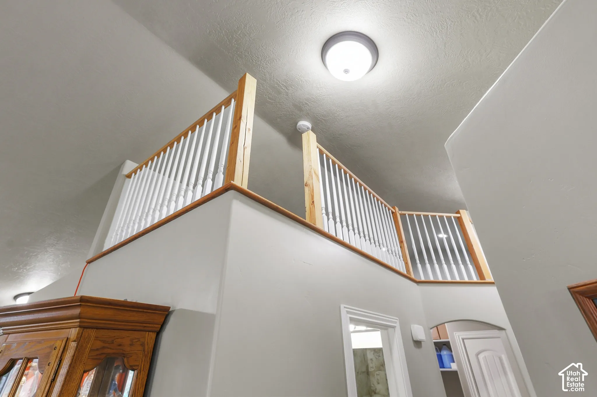 Elevated mezzanine featuring a natural wood-finish handrail and crisp white vertical balusters under a vaulted ceiling. Sellers used it as a space for their grandchildren to hide, but can also be used as storage.