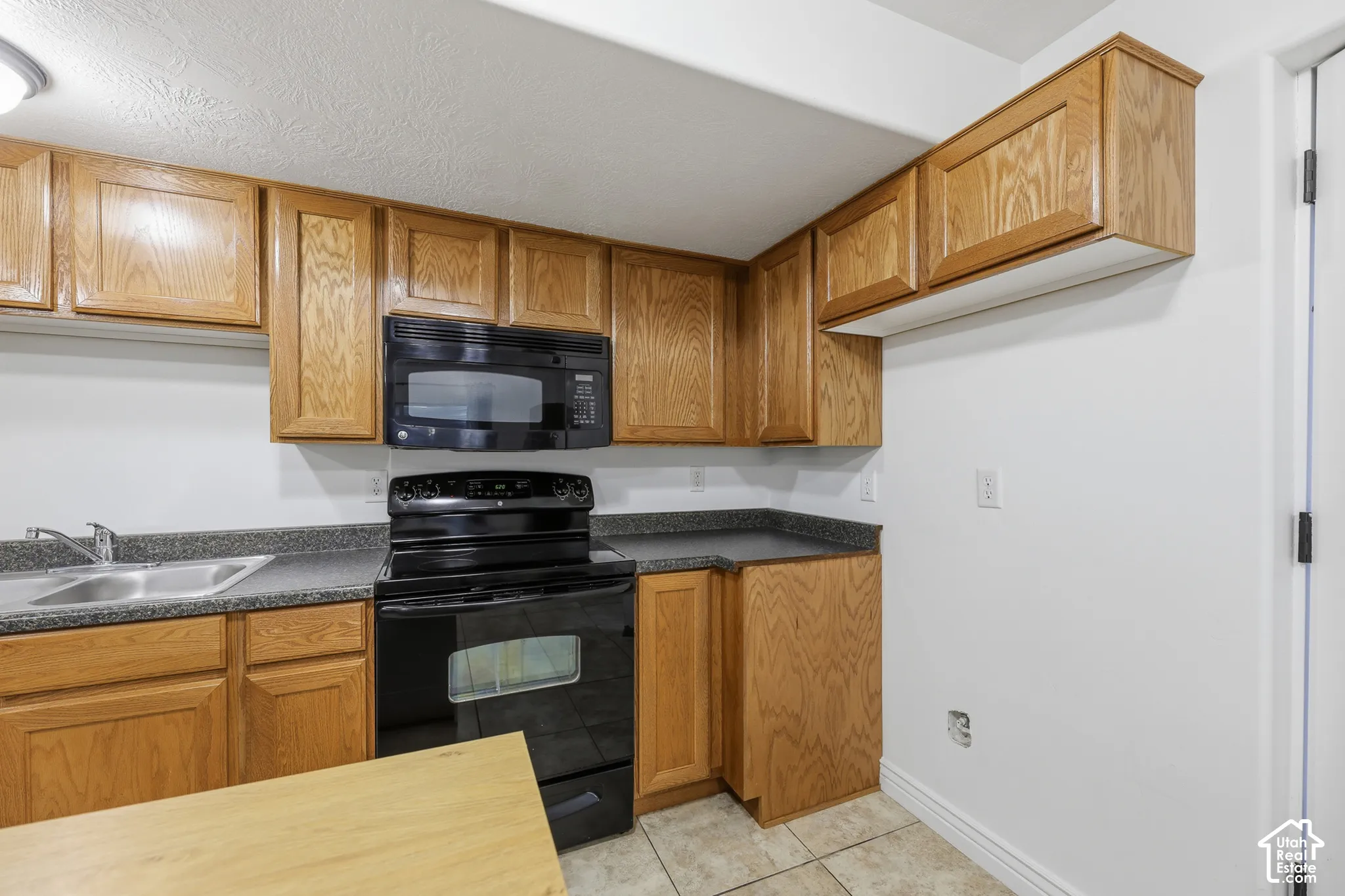 Kitchen featuring wood cabinetry, black appliances, dark stone-finish countertops, stainless steel dual-basin sink, and tile flooring