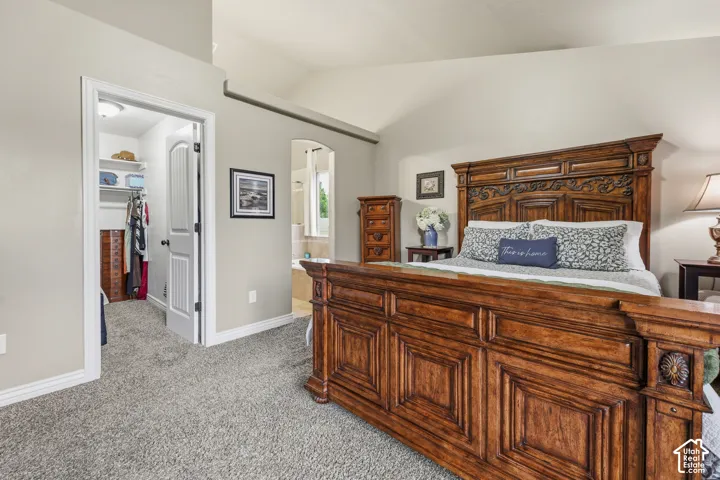Vaulted ceilings, neutral wall paint, carpeting, and an arched doorway leading to a secondary room