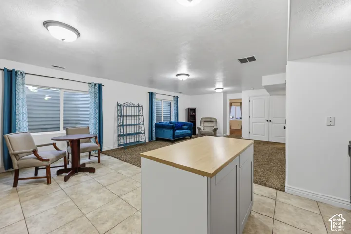 Open-concept interior featuring light-toned tile flooring, carpeted flooring, a center island with a wood-finish surface, recessed ceiling lighting, and double-panel doors