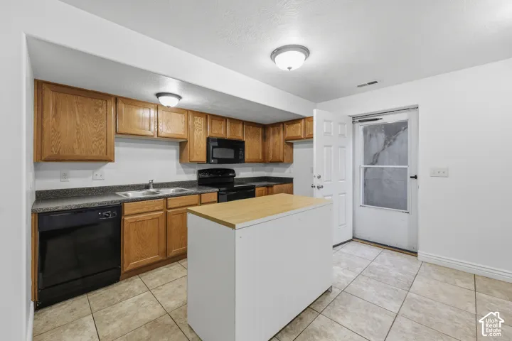 Kitchen featuring wood cabinetry, a center island with a wood-finish countertop, dark-toned appliances, solid-surface countertops, and tile flooring