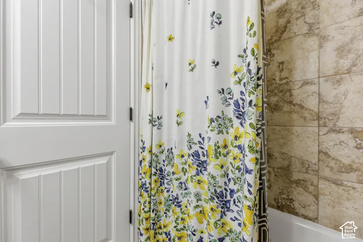 Elegant bathroom featuring a decorative shower curtain with blue and yellow floral patterning, polished chrome shower fixtures, and neutral tile flooring and surround walls in warm earth tones