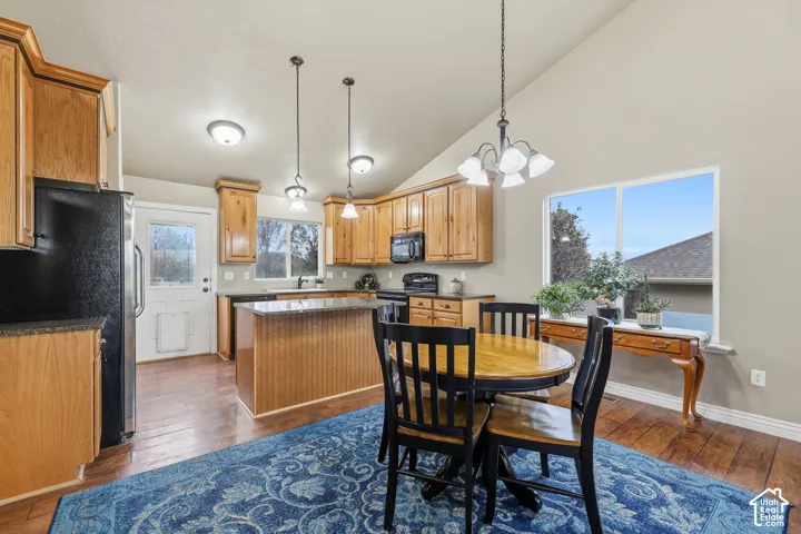 Kitchen featuring wood cabinetry, an island with dark countertops, wood-finish flooring, vaulted ceilings, and multi-light hanging fixtures