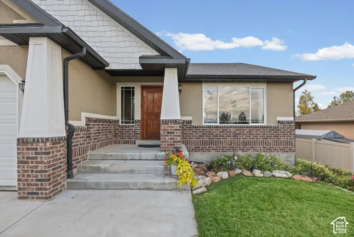 Exterior facade featuring a combination of stucco and masonry brick siding, shake-style gable detailing, a prominent covered entryway with tapered columns, and a wood-finish front door