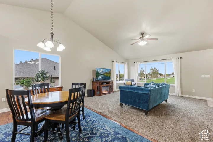 Vaulted ceilings, large windows with natural lighting, polished wood-finish flooring, a multi-light chandelier, and a ceiling fan