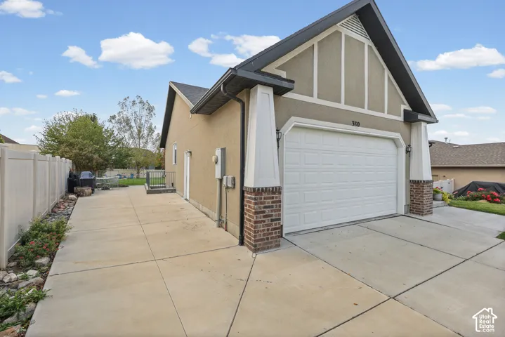 Stucco exterior featuring gable roofline, decorative timber framing, masonry pier detailing, and a concrete driveway