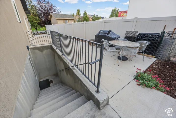 Concrete patio featuring a metal railing enclosure and a concrete stairwell leading to an exterior entrance, bordered by a vinyl privacy fence. Separate basement entrance.