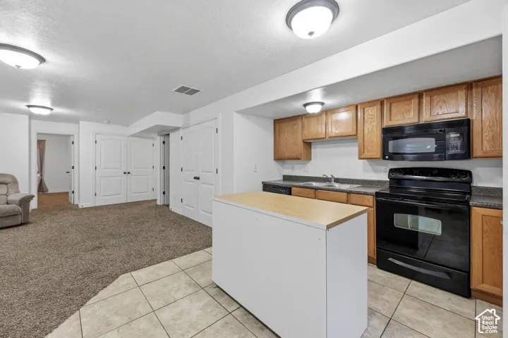 Kitchen featuring wood cabinetry, a standalone island with a wood-finish countertop, black appliances, tile flooring, and flush-mount ceiling lighting