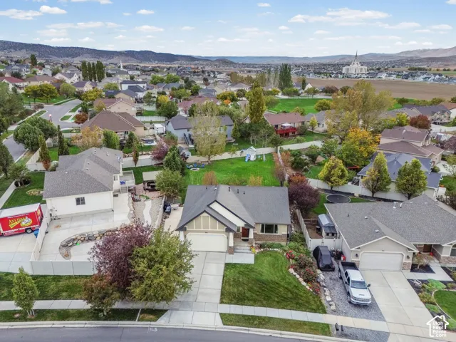 Aerial perspective of suburban residence featuring a concrete driveway, two-car garage, manicured front lawn, and mountain backdrop