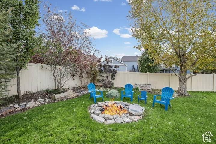 Backyard featuring a stone fire pit, vinyl privacy fencing, manicured lawn, and mature trees