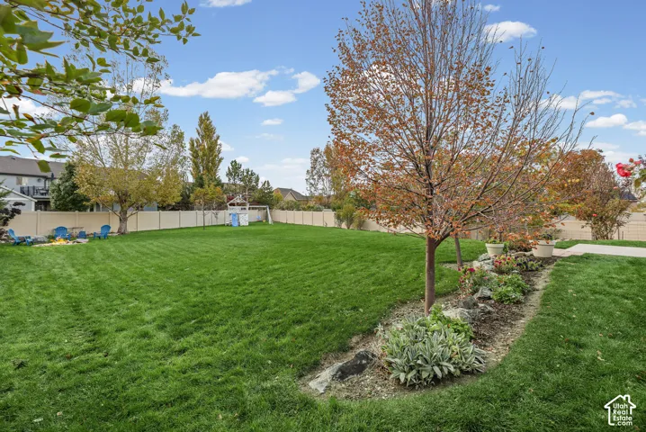 Spacious backyard featuring a manicured lawn, established landscaping, decorative rock edging, and a vinyl privacy fence