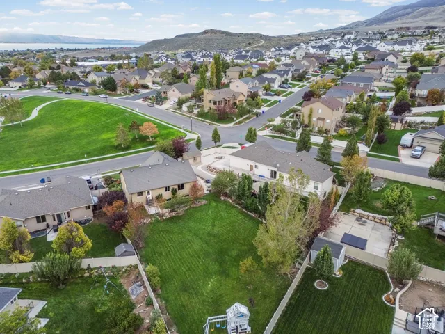 Aerial perspective featuring suburban residential surroundings with mountain backdrop, manicured lawns, mature trees, and paved street access