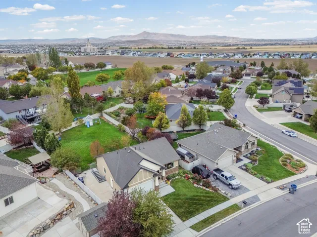 Aerial perspective of residential property featuring a multi-pitched roofline, attached multi-car garage, fenced backyard, and surrounding mountain scenery