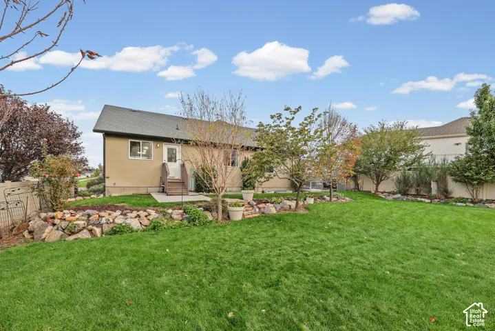 Expansive backyard featuring a manicured lawn, stone terracing, mature trees, and a concrete patio