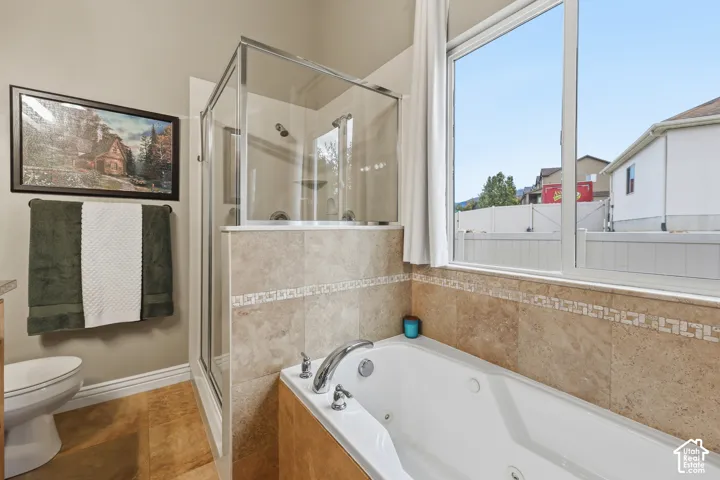 Jetted soaking tub with chrome fixtures, glass-enclosed shower, stone-tile backsplash, and natural-tone stone flooring