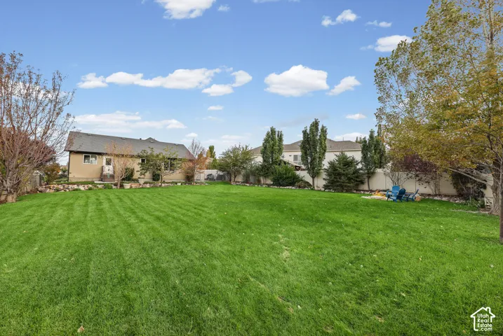 Expansive backyard featuring a large grass lawn, mature trees, stone landscaping borders, and perimeter fencing