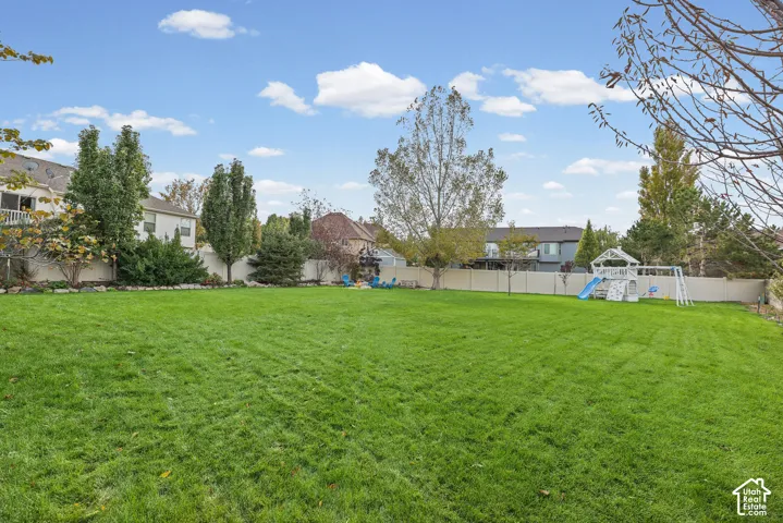 Expansive backyard featuring a manicured lawn, perimeter fencing, and mature trees