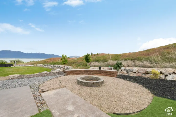 Outdoor fire pit featuring stone masonry construction, integrated curved retaining wall seating, gravel hardscaping, and natural rock terracing with mountain and water backdrops