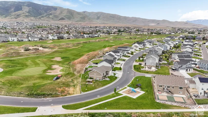 Aerial perspective of a residential neighborhood featuring expansive green space, surrounding mountain topography, paved streets, and a recreational play area