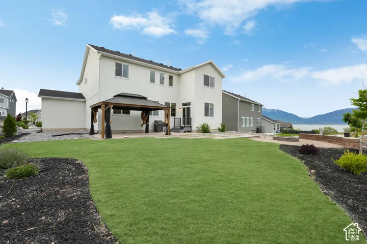 Rear exterior featuring a stucco facade, covered metal-roof gazebo, concrete patio, stone fire pit, and a landscaped lawn with mountain backdrop