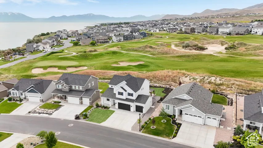 Aerial perspective of suburban residential properties featuring multi-level architecture, paved driveways, attached garages, and proximity to expansive golf course fairways
