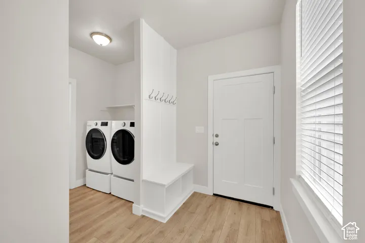 Mudroom featuring wood-finish flooring, white built-in cabinetry with cubby seating, wall-mounted hooks, and a laundry area with overhead shelving