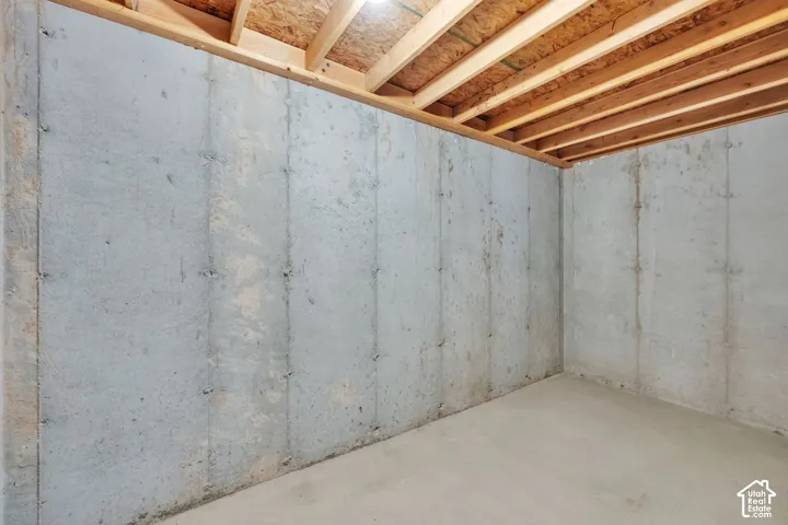Unfinished room featuring poured concrete walls, a concrete floor, and exposed wooden ceiling joists