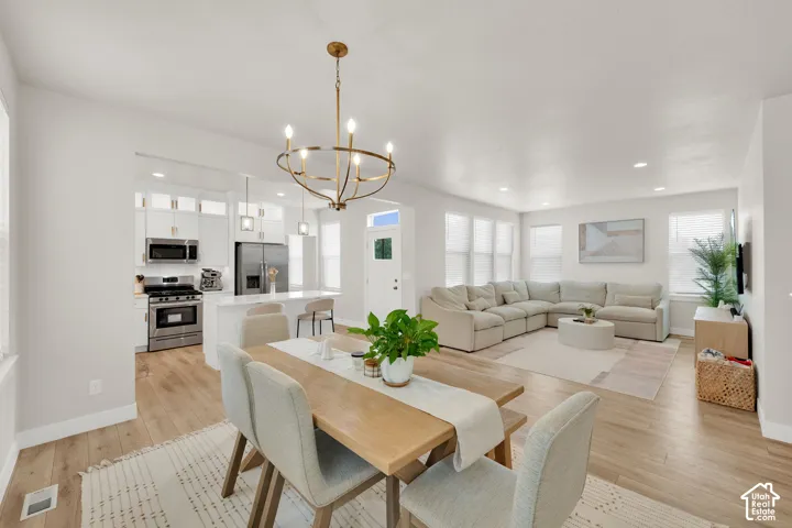 Open-concept layout featuring wood-finish flooring, white cabinetry, integrated stainless steel appliances, quartz countertops, and a modern metal chandelier
