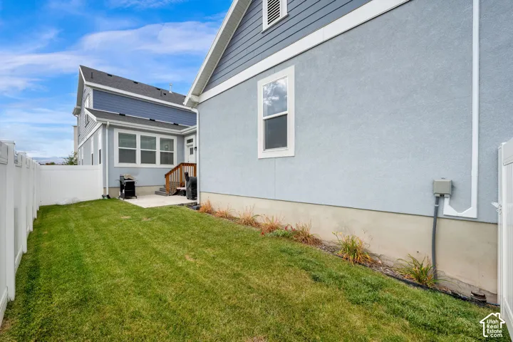 Exterior side yard featuring a manicured lawn, concrete patio, white vinyl perimeter fencing, and a combination of stucco and horizontal siding finishes