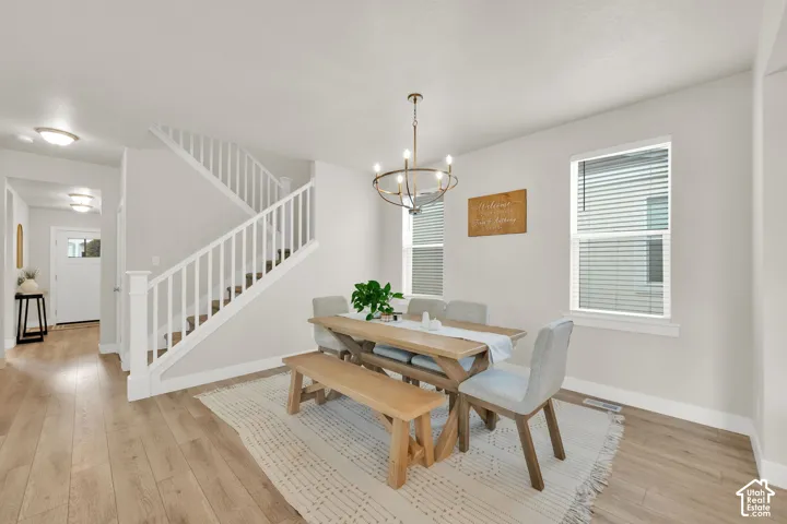 Dining area featuring wood-finish flooring, a multi-arm metal chandelier, white wooden staircase railings, and dual windows with horizontal blinds