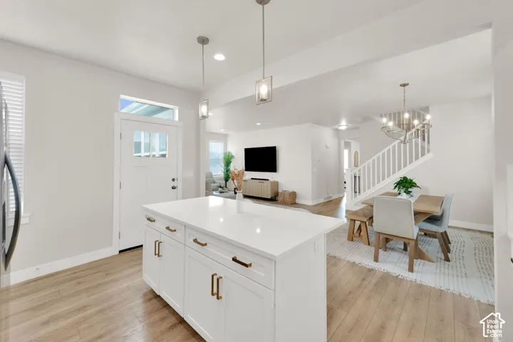 Kitchen island featuring white cabinetry with metallic pulls and a quartz countertop, complemented by wood-finish flooring, two pendant light fixtures, and a white staircase with a wooden railing