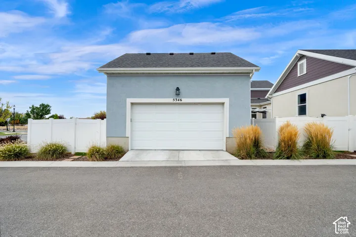 Detached garage featuring a stucco exterior, asphalt shingle roof, concrete apron, and white vinyl perimeter fencing